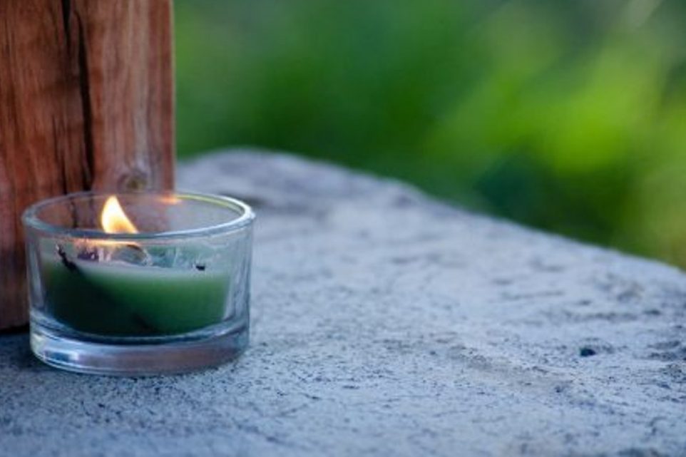 A burning green candle in the small jar put outside on the stone