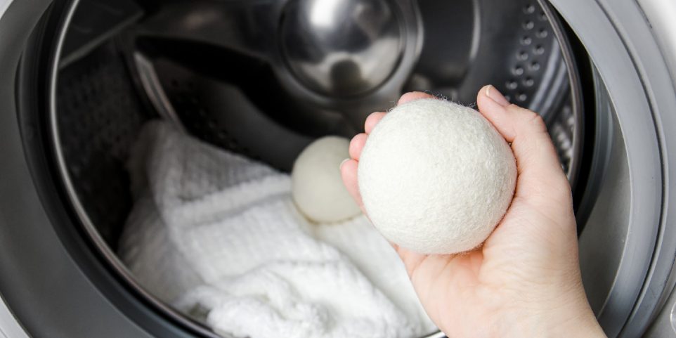 Woman using wool dryer balls for more soft clothes while tumble drying in washing machine concept