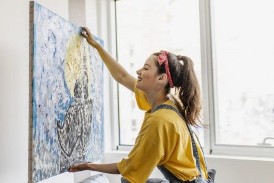 Young woman hanging art picture on wall and decorating living room